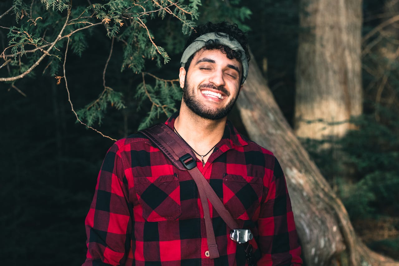 services-01 A joyful man in a red plaid shirt smiling in a forest setting.